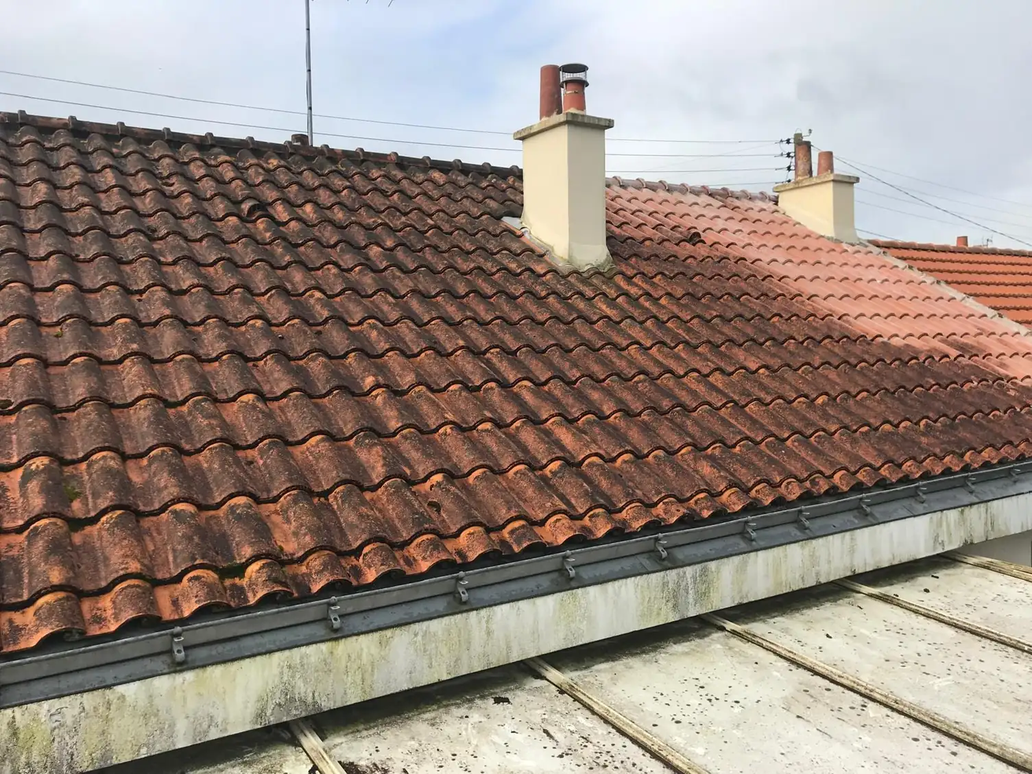 Toiture en tuiles et souche de cheminée vues depuis une terrasse